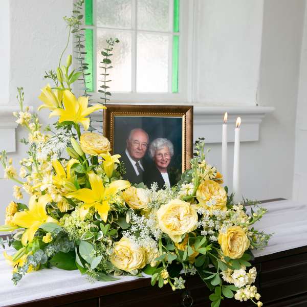Yellow floral arrangement beside a framed photo and candles on a casket
