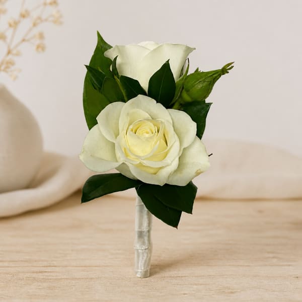 White rose boutonniere with dark green leaves and a wrapped stem
