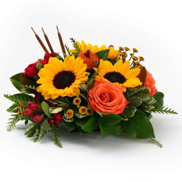 Low autumn centerpiece with bright yellow sunflowers, orange roses, red spray roses, and small pumpkins.