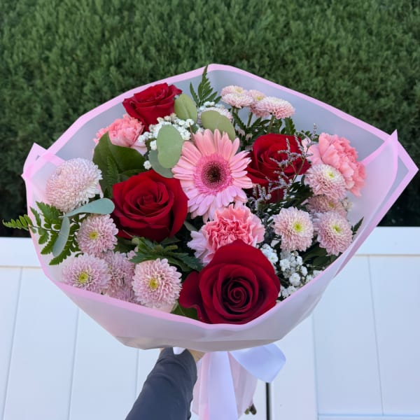 Bouquet of red roses, pink gerberas, and pale pink mums wrapped in pink paper