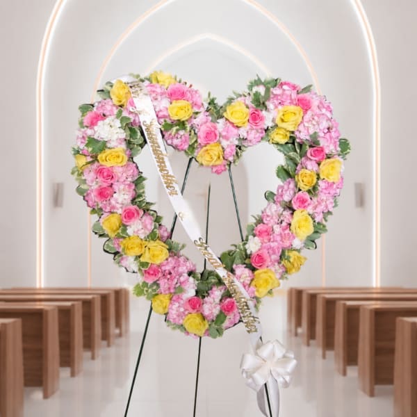 Heart-shaped floral wreath with pink and yellow roses on a stand