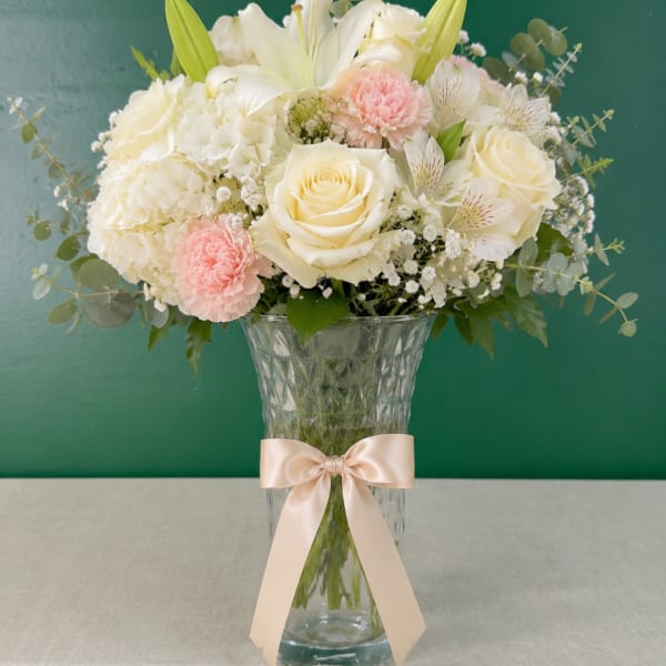 Cream and blush bouquet in a clear vase with a satin ribbon