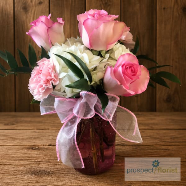 Pink roses and white hydrangeas in a purple glass vase with a pink ribbon