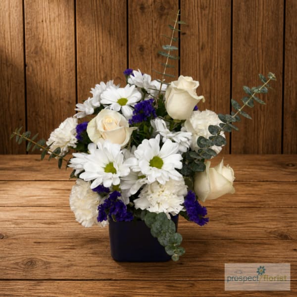 White roses and daisies in a dark square vase with purple accents