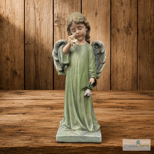 Angel figurine in a green robe holding a flower on a wooden background