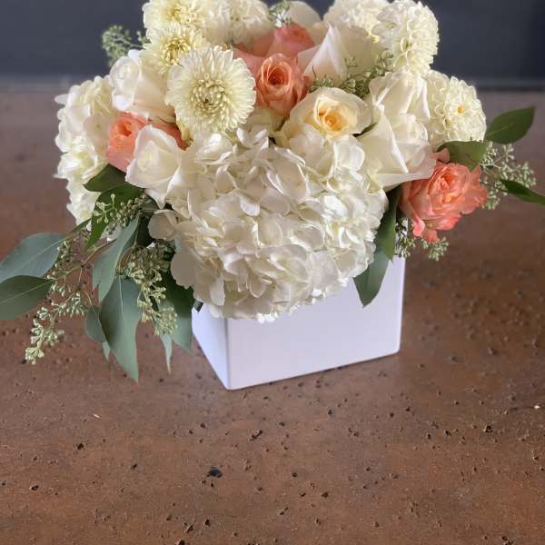 White and peach floral arrangement in a white square vase