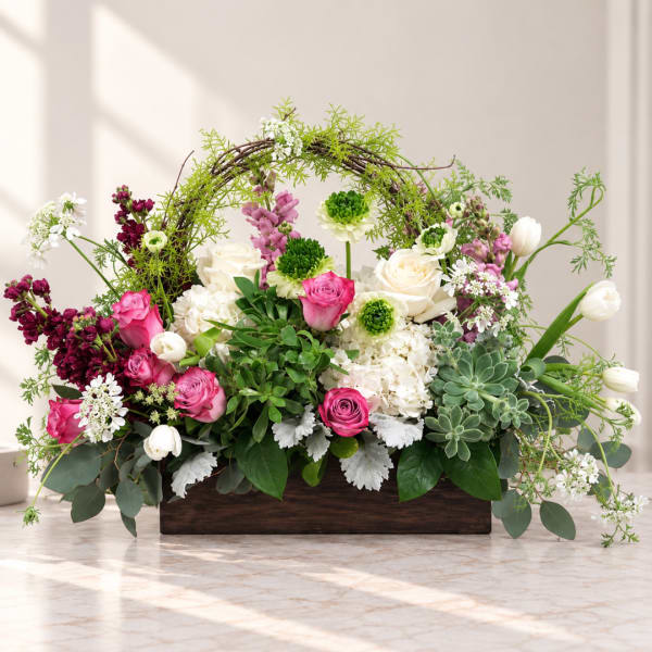 Mixed pink and white flowers arranged in a wooden box with a vine arch