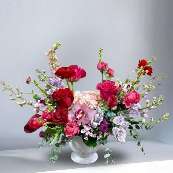 Mixed bouquet of red, pink, and lavender flowers in a white vase