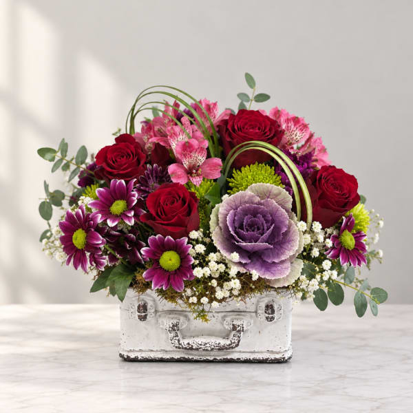 Mixed bouquet in a white suitcase-style container with red roses and purple flowers