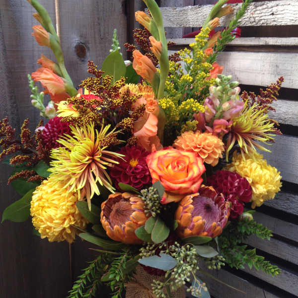 Colorful bouquet with orange roses and yellow chrysanthemums in a burlap-wrapped vase