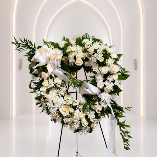 White floral wreath with roses and ribbon on a stand