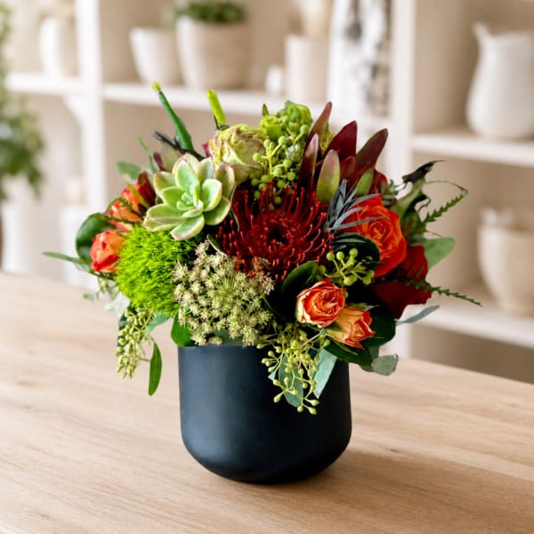 Mixed floral arrangement in a black vase with succulents and orange-red blooms
