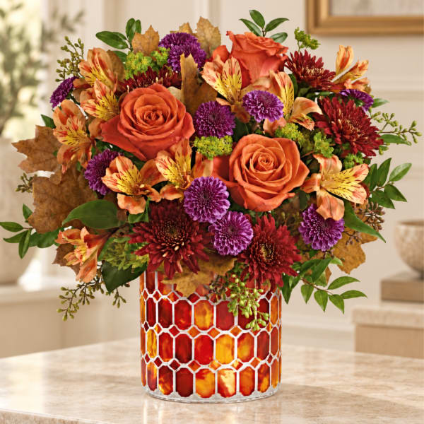 Orange roses and mixed fall flowers in a patterned glass vase