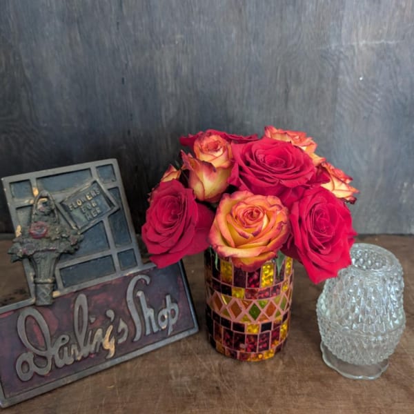 Red and yellow roses in a mosaic glass vase beside decorative plaques