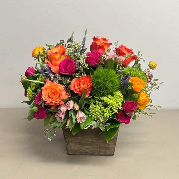 Mixed bouquet of orange, pink, and yellow flowers in a wooden container