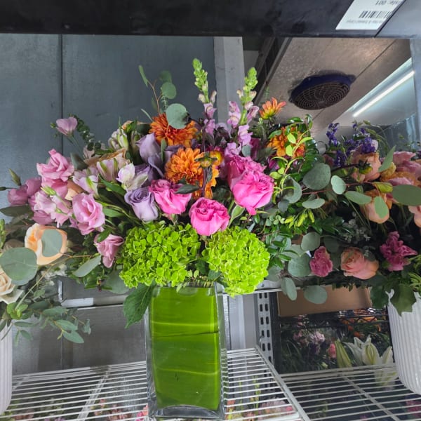 Mixed bouquet in a tall green glass vase with pink, purple, and orange flowers
