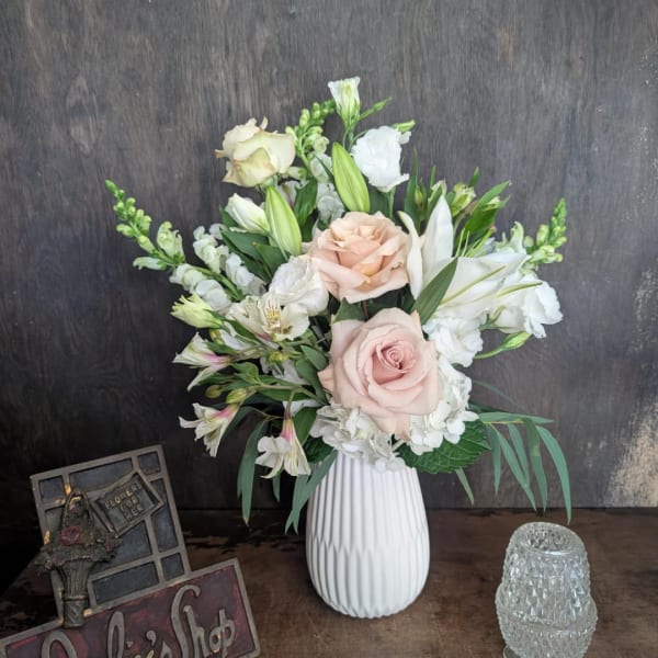 Blush roses and white lilies arranged in a white vase