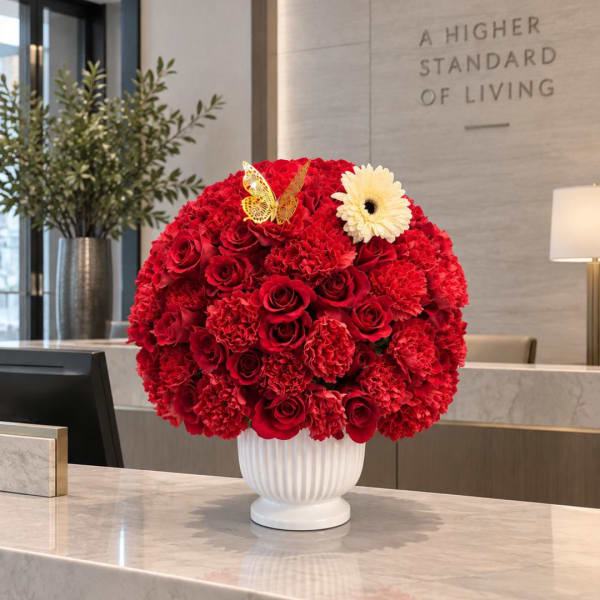 Round red floral arrangement in a white vase with a white daisy and butterfly accent