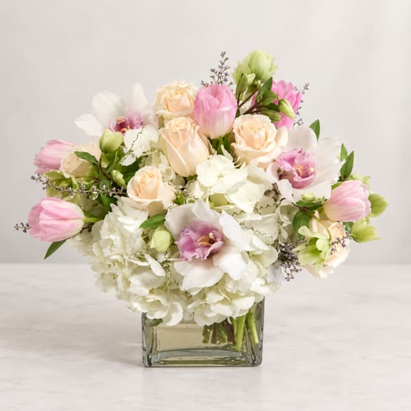 Wedding bouquet of pink tulips, cream roses, and white orchids in a glass vase