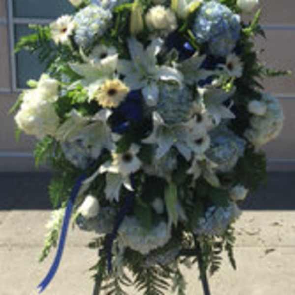 Blue and white funeral spray with lilies, hydrangeas, and ribbon