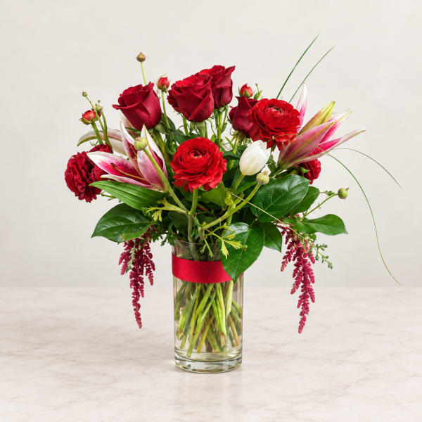 Red roses and lilies arranged in a clear glass vase with a red ribbon
