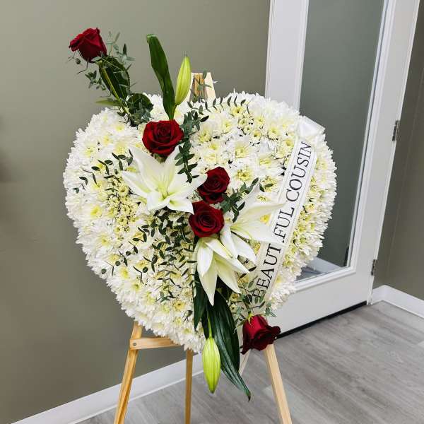 Heart-shaped white floral wreath with red roses and lilies on an easel