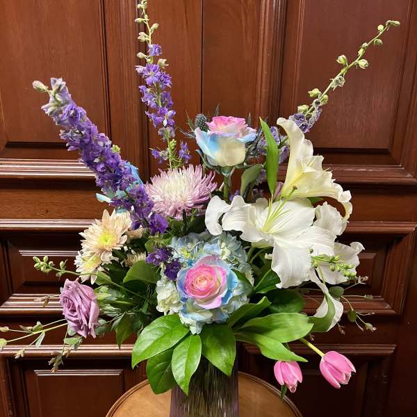 Tall mixed bouquet with lilies, roses, and purple blooms in a glass vase