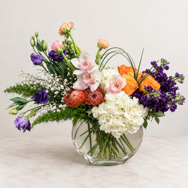 Mixed bouquet of orchids, roses, hydrangea, and purple blooms in a glass vase