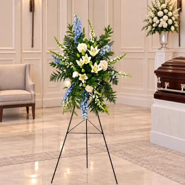 Standing funeral spray with white lilies, roses, and blue flowers on an easel