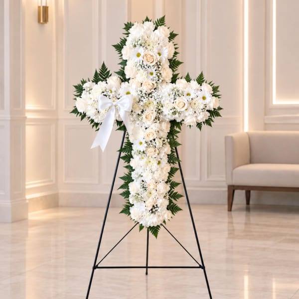 White floral cross on a black stand with a ribbon bow