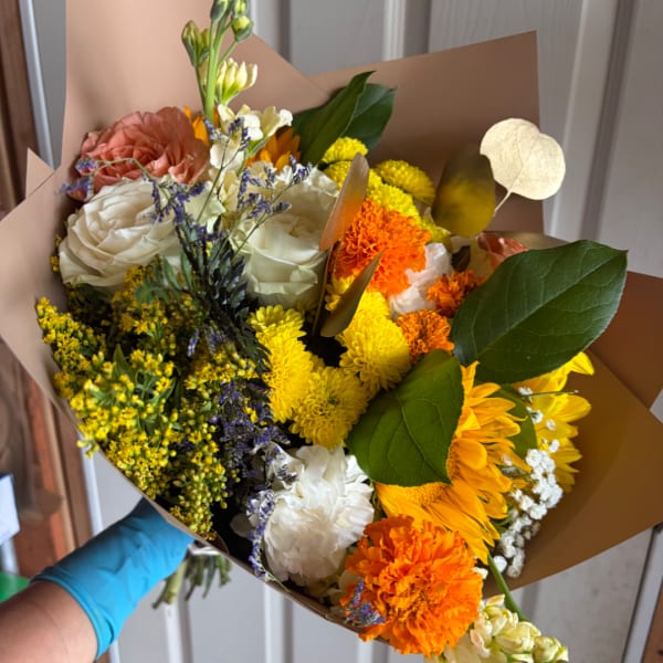Mixed bouquet of roses, chrysanthemums, and carnations wrapped in brown paper