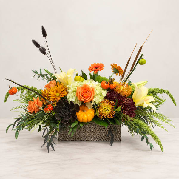 Autumn floral arrangement in a rectangular vase with orange, yellow, and dark blooms