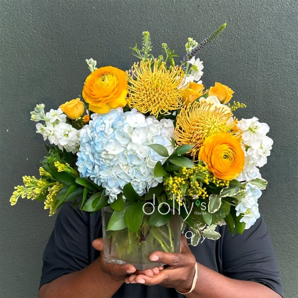 Mixed bouquet in a clear glass vase with blue hydrangea, orange blooms, and white flowers