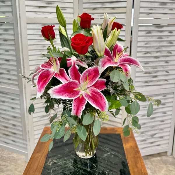 Bouquet of pink lilies and red roses in a clear glass vase