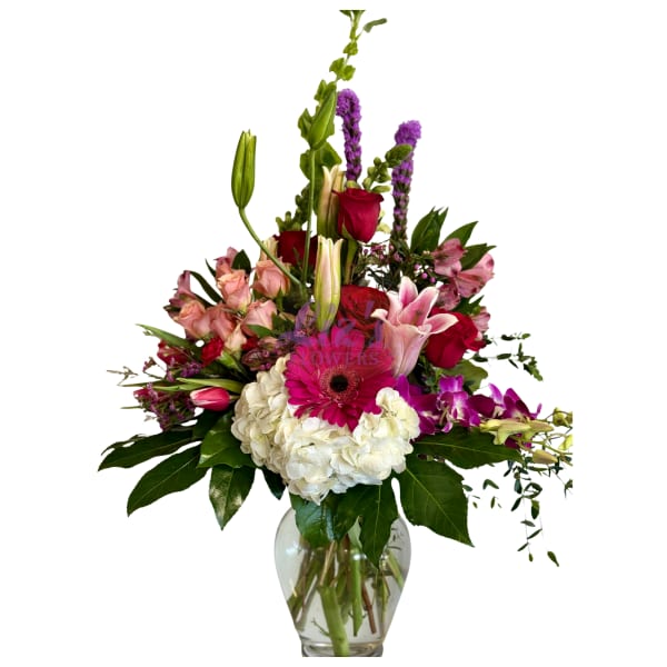 Mixed bouquet of pink, red, white, and purple flowers in a clear glass vase