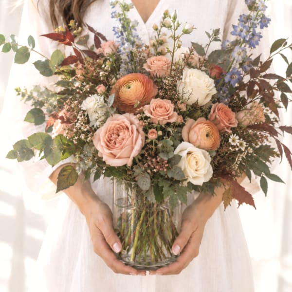 Mixed bouquet of blush roses, white blooms, and blue flowers in a glass vase