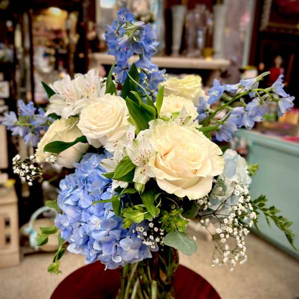Bouquet of cream roses, blue hydrangeas, and white flowers in a glass vase