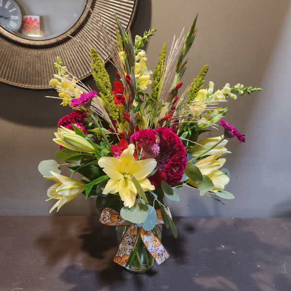 Mixed bouquet with yellow lilies, red and magenta blooms in a glass vase