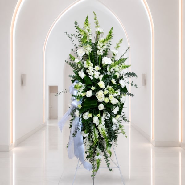 Tall white floral standing spray with ribbon in a bright hallway