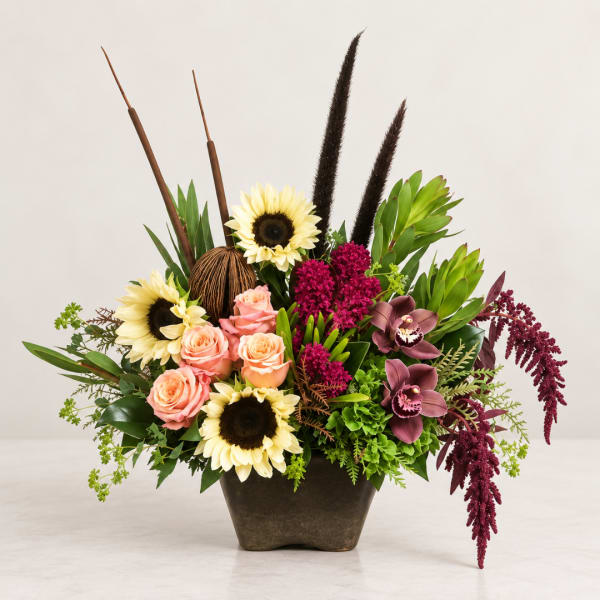 Mixed floral arrangement in a dark vase with sunflowers, roses, and orchids