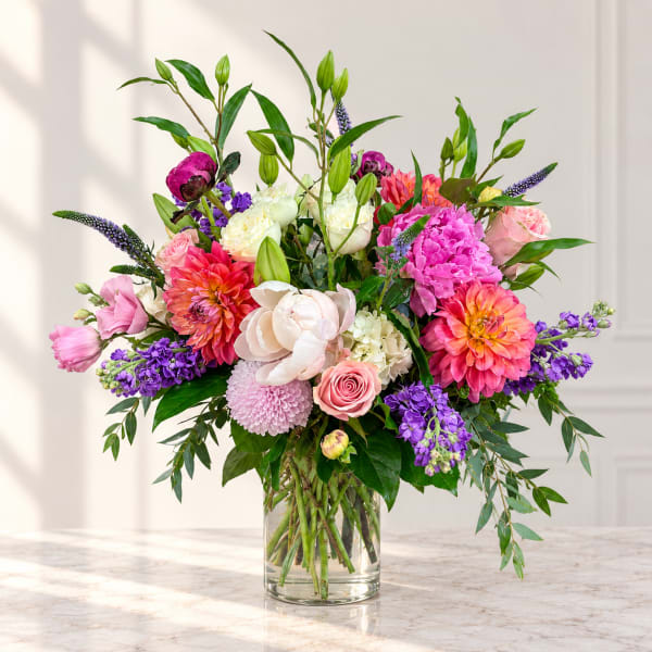 Mixed bouquet of pink, purple, white, and orange flowers in a clear glass vase