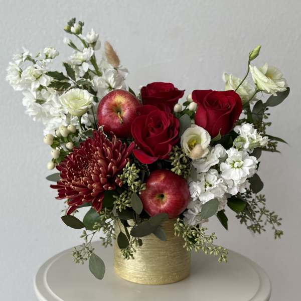 Red roses and white flowers arranged in a gold vase with apples