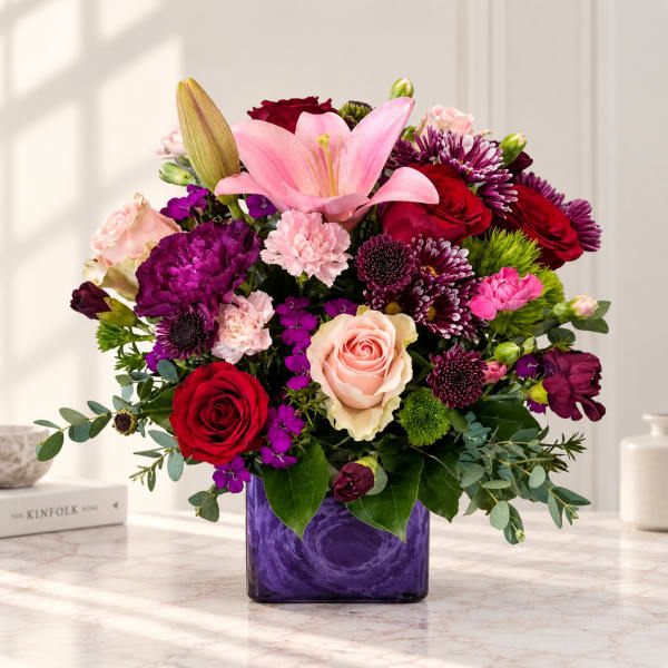 Mixed bouquet of pink, red, and purple flowers in a purple vase