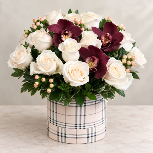 White roses and burgundy orchids in a plaid hatbox container