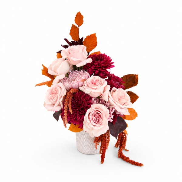Pink and burgundy flowers arranged in a white vase with orange leaves