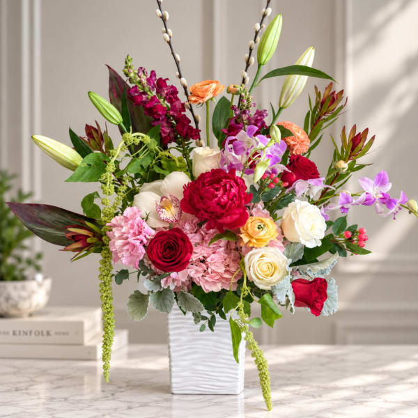 Mixed bouquet in a white vase with roses, orchids, lilies, and pink blooms