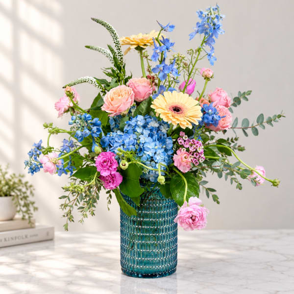 Mixed bouquet of pink, blue, and yellow flowers in a blue glass vase