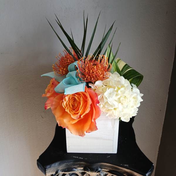 Orange rose and white hydrangea arrangement in a white box with blue ribbon