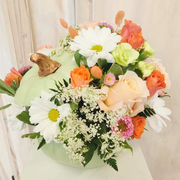 Mixed bouquet with daisies, roses, and small filler flowers in a pale green container