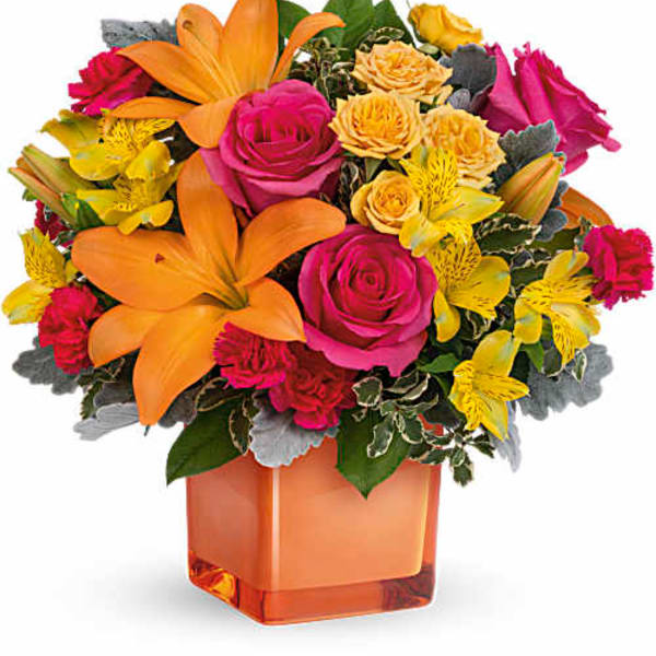 Bright mixed bouquet in an orange square vase with pink roses and orange lilies
